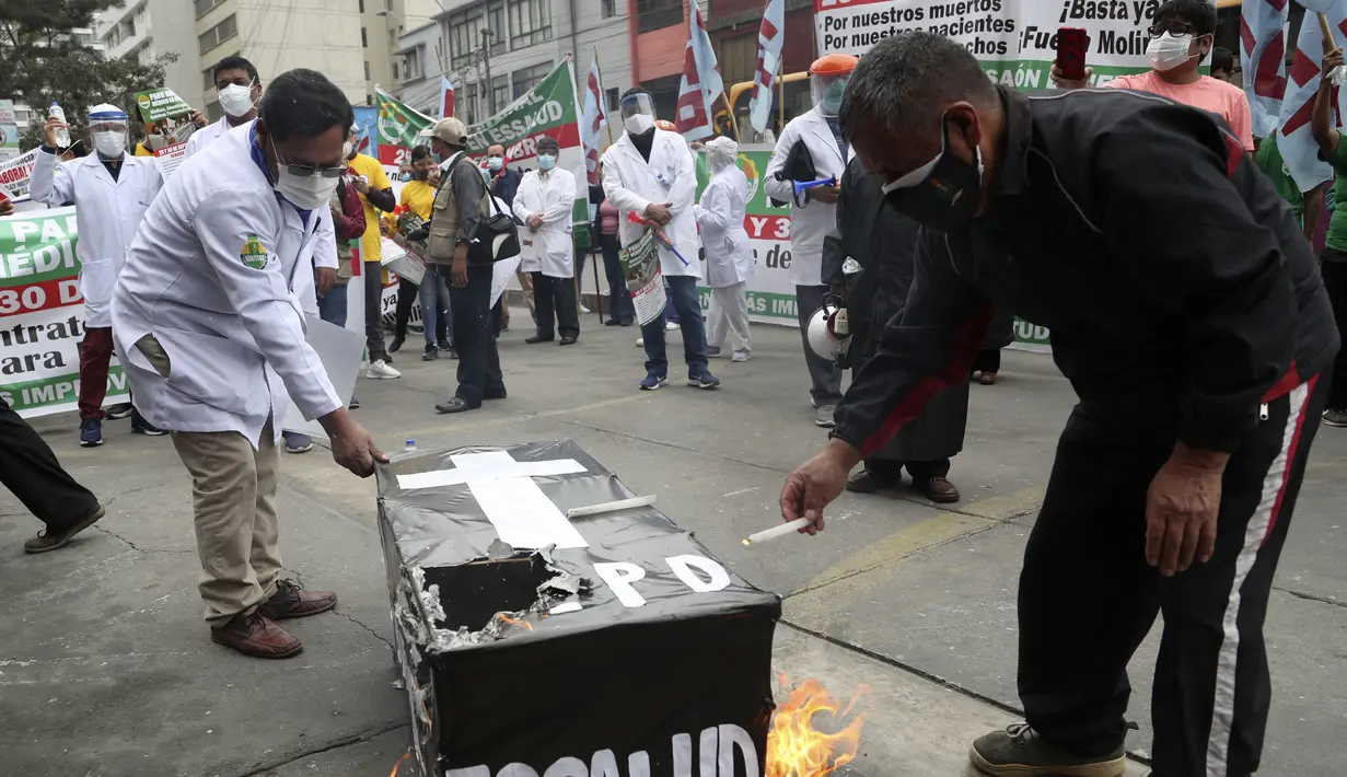 Petugas kesehatan membakar peti mati palsu saat mereka memprotes kurangnya alat pelindung bagi mereka yang merawat pasien COVID-19, di luar rumah sakit umum di Lima, Peru (29/9/2020). (AP Photo/Martin Mejia)