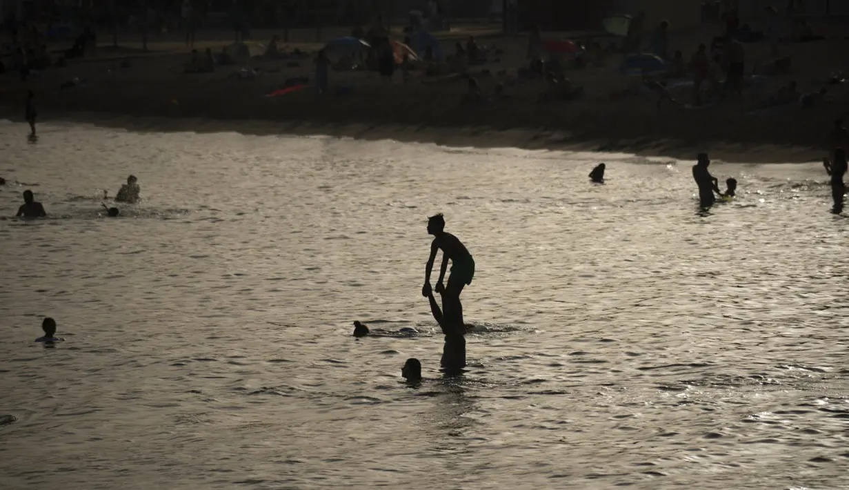 Orang-orang bermain dan bersantai di laut di tepi pantai di Barcelona, Spanyol, Kamis (12/8/2021). Bagian timur laut Spanyol, di wilayah Catalonia, diperkirakan mencapai 42 derajat Celcius pada hari Kamis. (AP Photo/Joan Mateu Parra)