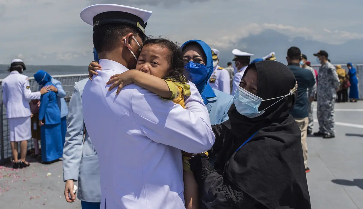 Seorang perwira angkatan laut memeluk seorang anak Upacara Tabur Bunga di geladak heli KRI Dr. Soeharso 990 di perairan utara Pulau Bali, Bali, Jumat (30/4/2021). Upacara itu digelar sebagai penghormatan terakhir bagi awak KRI Nanggala 402 yang gugur dalam medan tugas. (Juni Kriswanto/AFP)
