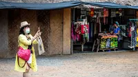 Seorang turis yang mengenakan masker mengambil gambar di luar kios suvenir di Taman Chang Siam, Pattaya, Thailand, Rabu (12/2/2020). Chang Siam Park adalah salah satu primadona bagi wisatawan China di Pattaya  yang kini berangsur sepi karena penyebaran virus corona covid-19. (Mladen ANTONOV / AFP)