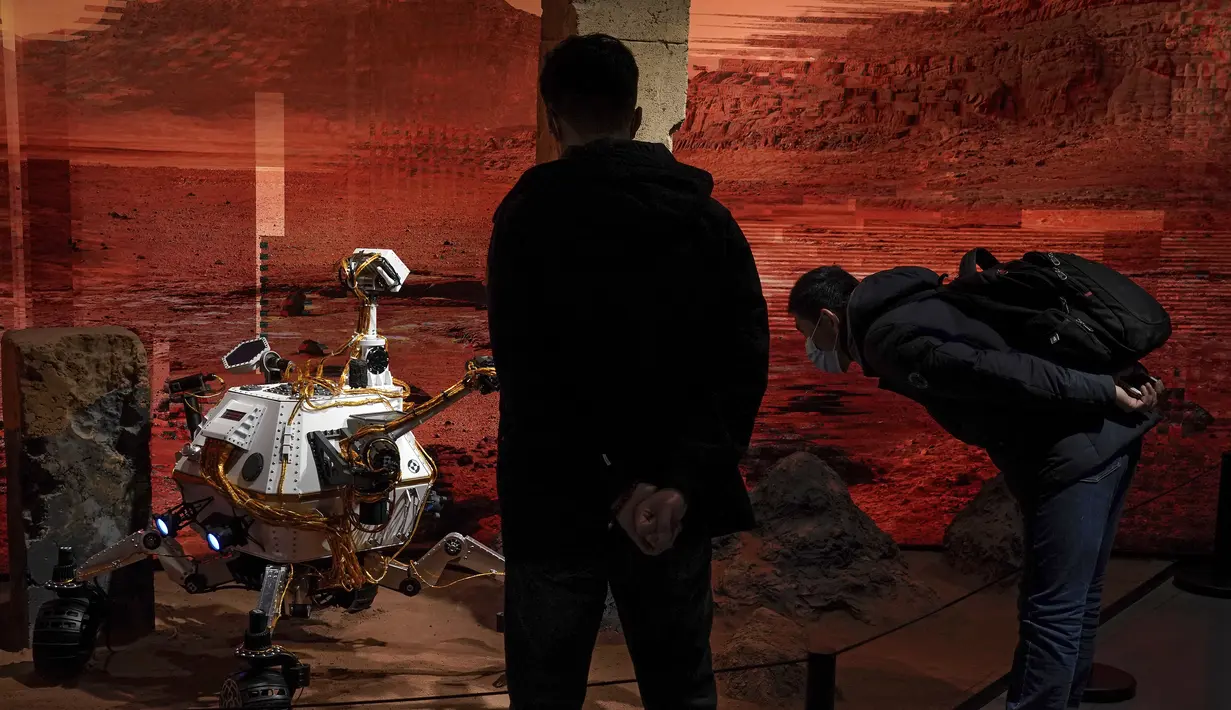 Pengunjung mengenakan masker untuk mencengah penyebaran Covid-19 melihat model yang menggambarkan penjelajah di Mars selama pameran di sebuah pusat perbelanjaan di Beijing, Rabu, (24/2/2021).  China mengatakan pesawat ruang angkasa Tianwen-1 telah memasuki masa temporer. (AP Photo/Andy Wong)