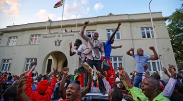 Warga Zimbabwe bergembira setelah kabar Presiden Robert Mugabe mengundurkan diri di luar gedung parlemen, pusat kota Harare, Selasa (21/11). Surat pengunduran diri Robert Mugabe itu mengakhiri masa pemerintahannya selama 37 tahun. (AP/Ben Curtis)