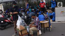Pedangang menyiapkan makanan untuk massa aksi saat demo penolakan omnibus law di kawasan Patung Kuda, Jakarta, Selasa (20/10/2020). Para pedagang kaki lima memanfaatkan moment aksi massa untuk mencari ke untungan meskipun sangat membahayakan bagi keselamatan mereka. (Liputan6.com/Angga Yuniar)