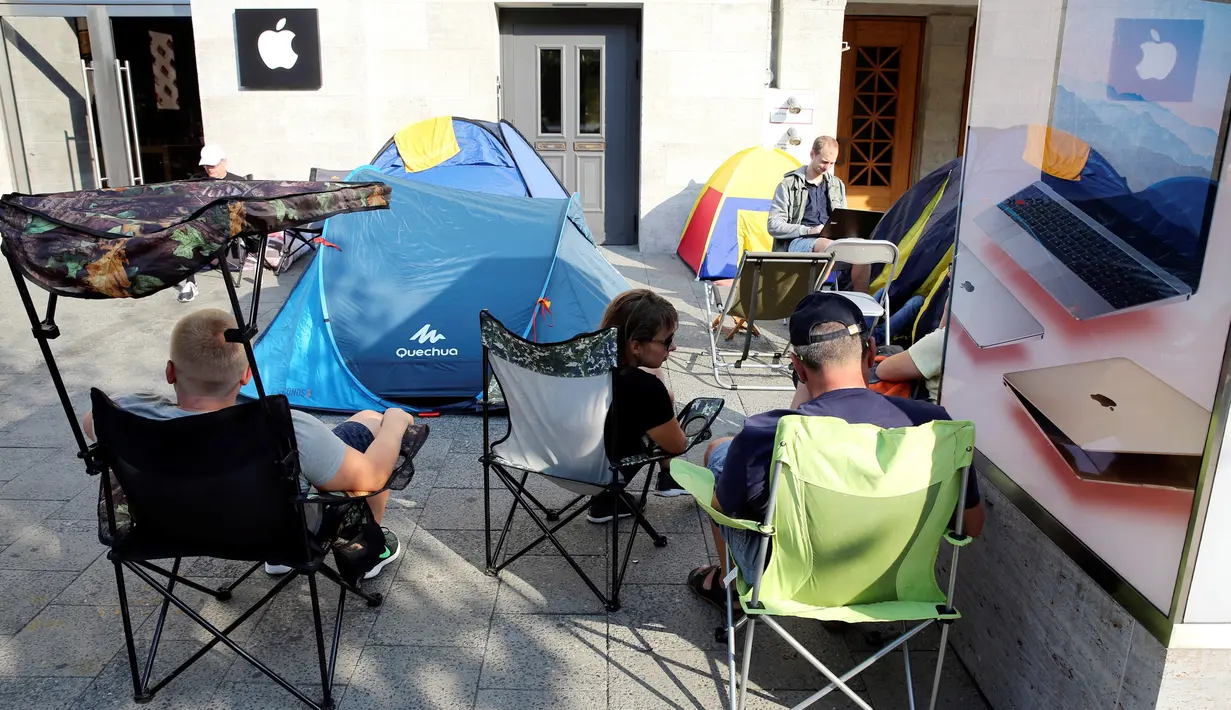 Pecinta iPhone sedang berbincang dan membuka laptop di samping tenda mereka di depan toko Apple Berlin, Jerman (12/09). Selain di Berlin, antrean calon pembeli iPhone 7 juga sudah terlihat di kota New York. (REUTERS/Fabrizio Bensch)