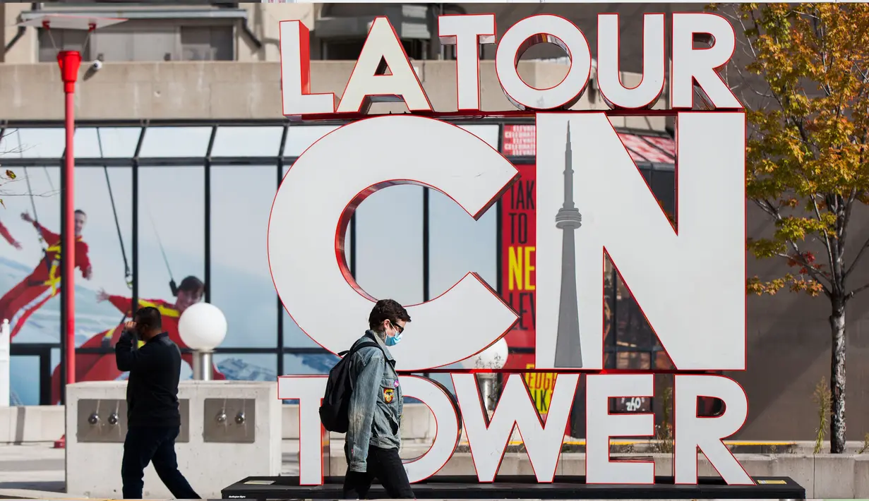 Seorang pria yang memakai masker berjalan melewati papan nama CN Tower di Toronto, Kanada, pada 3 Oktober 2020. CN Tower kembali ditutup untuk umum pada Sabtu (3/10) di tengah melonjaknya kasus COVID-19. (Xinhua/Zou Zheng)