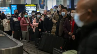 Pelancong yang memakai masker menunggu barang bawaan mereka di area kedatangan internasional di Bandara Internasional Ibukota Beijing di Beijing, Senin (9/1/2023). Pelancong internasional pertama tiba di China tanpa karantina wajib yang telah diberlakukan pada awal penerbangan. Pandemi tiga tahun lalu setelah pembatasan dicabut mulai hari Minggu. (AP/Mark Schiefelbein)