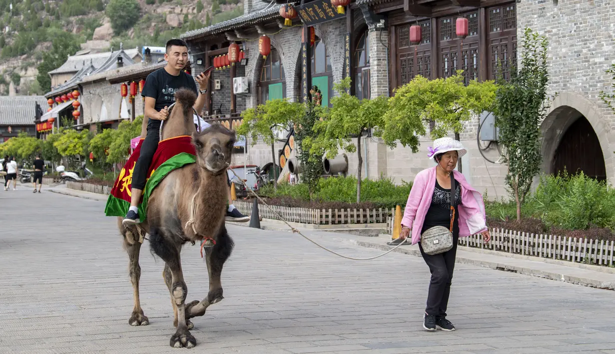 Seorang wisatawan menaiki seekor unta di kota kuno Qikou di Wilayah Linxian, Lyuliang, Provinsi Shanxi, China utara, pada 9 Juni 2020. (Xinhua/Yang Chenguang)