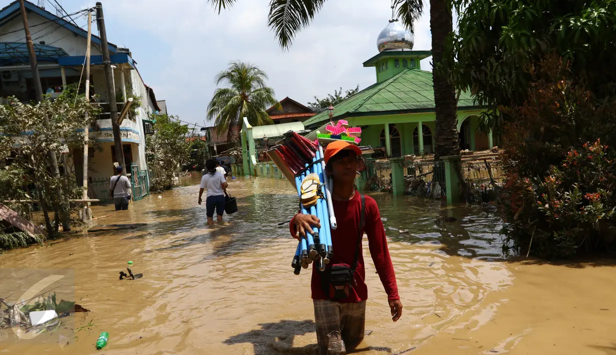 Seorang pedagang melewati banjir sambil membawa dagangannya di kompleks Pondok Gede Permai, Jatiasih, Bekasi, Jumat (22/4). Pedagang berjualan alat kebersihan untuk membersihkan sisa lumpur yang terbawa banjir di kawasan itu. (Liputan6.com/Fery Pradolo)