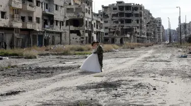 Pengantin baru, Nada Merhi (18) dan Hassan Youssef (27) menjalani sesi foto di kota Homs yang jadi medan perang di Suriah, 5 Februari 2016. Foto ini seolah bukti meski di tengah kehancuran, hidup terus berlalu dan harapan akan terus ada. (JOSEPH EID/AFP)
