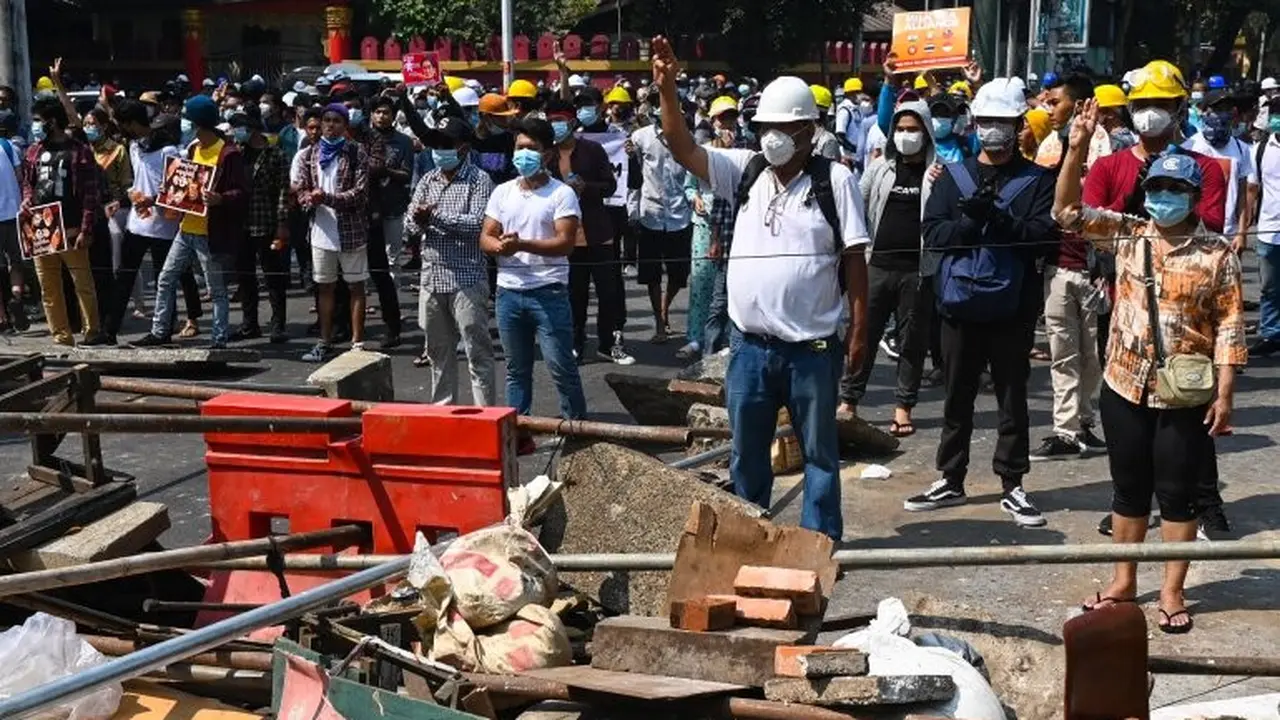 Para pengunjuk rasa memberi hormat tiga jari saat mereka berdiri di belakang barikade darurat selama demonstrasi menentang kudeta militer di Yangon pada 28 Februari 2021 [Ye Aung Thu / AFP]