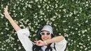 Maudy Ayunda terlihat cantik mengenakan busana kasual. Dalam foto ini, Maudy Ayunda berbaring di rumput dengan bunga-bunga putih mengenakan kaus putih, dilapisi dengan kemeja lengan panjang yang juga berwarna putih, dipadu dengan celana biru, bucket hat, dan sunglasses. Foto: Instagram.
