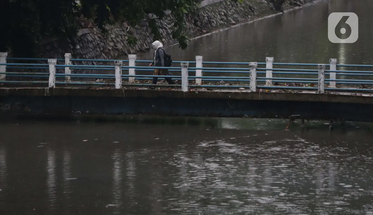 Warga melintasi jembatan penyeberangan kali di  kawasan Kuningan, Jakarta, Kamis (18/12/2021). BMKG memprakirakan potensi hujan lebat yang mungkin disertai petir dan angin kencang hingga 21 Februari di beberapa provinsi di Indonesia, termasuk DKI Jakarta. (Liputan6.com/Helmi Fithriansyah)