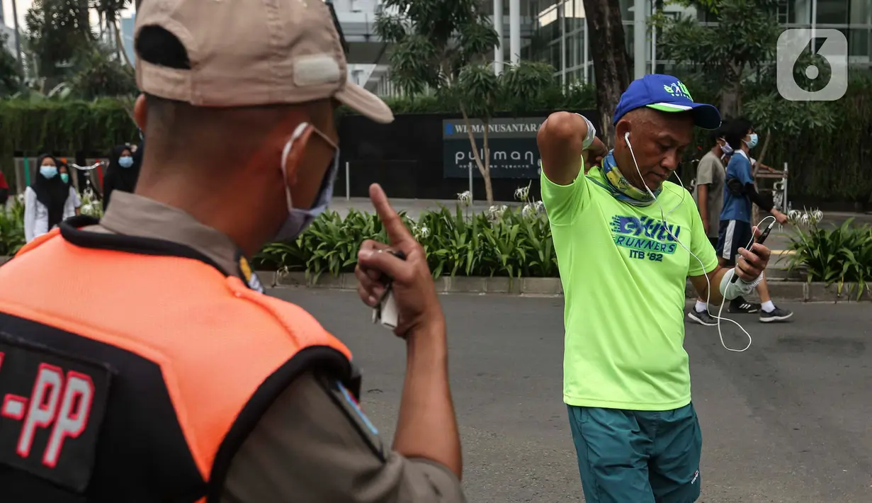Satpol PP menegur warga yang berolahraga tidak mengenakan masker dengan benar di kawasan Bundaran HI, Jakarta, Minggu (17/1/2021). Sosialisasi penggunaan masker untuk mencegah penularan virus corona COVID-19 masih saja diabaikan karena rendahnya kesadaran masyarakat. (Liputan6.com/Johan Tallo)