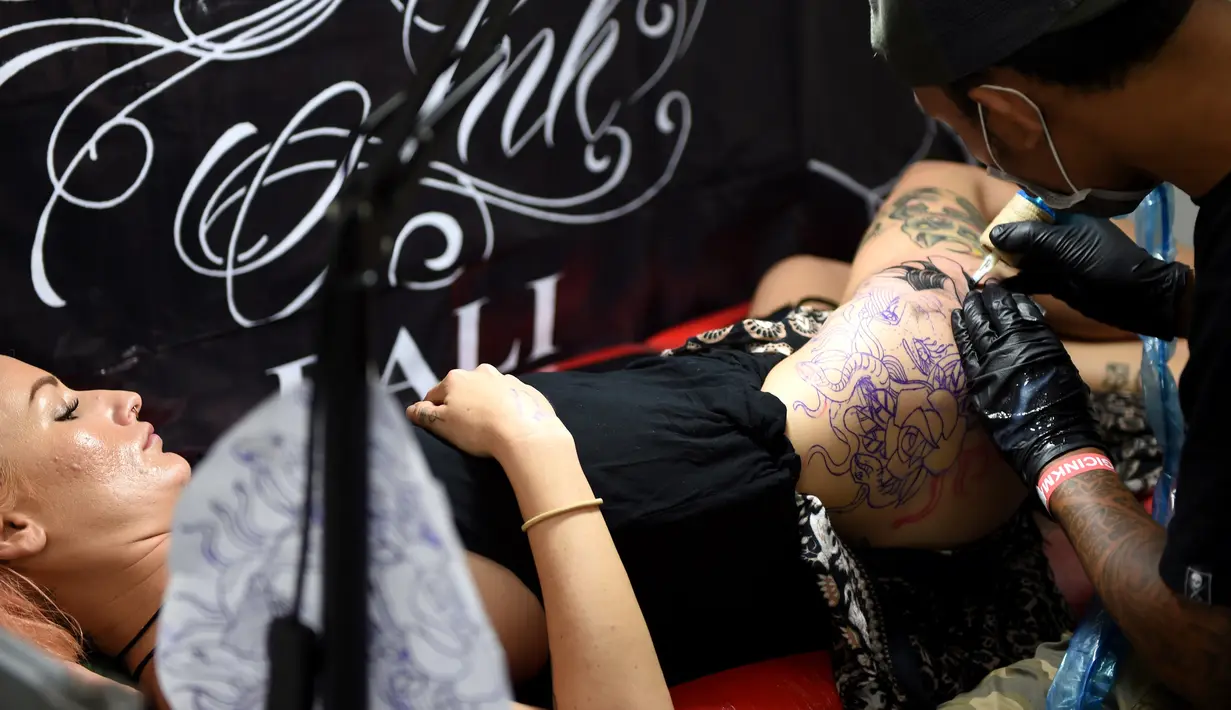 Seorang wanita saat dibuatkan tato dibagian pahanya oleh seniman dalam acara Bali Tattoo Expo 2017 di pulau resor Indonesia, Denpasar, Bali (12/5). Acara ini digelar selama 3 hari, mulai (12/5/2017) sampai (14/5/2017). (AFP Photo/Sonny Tumbelaka)