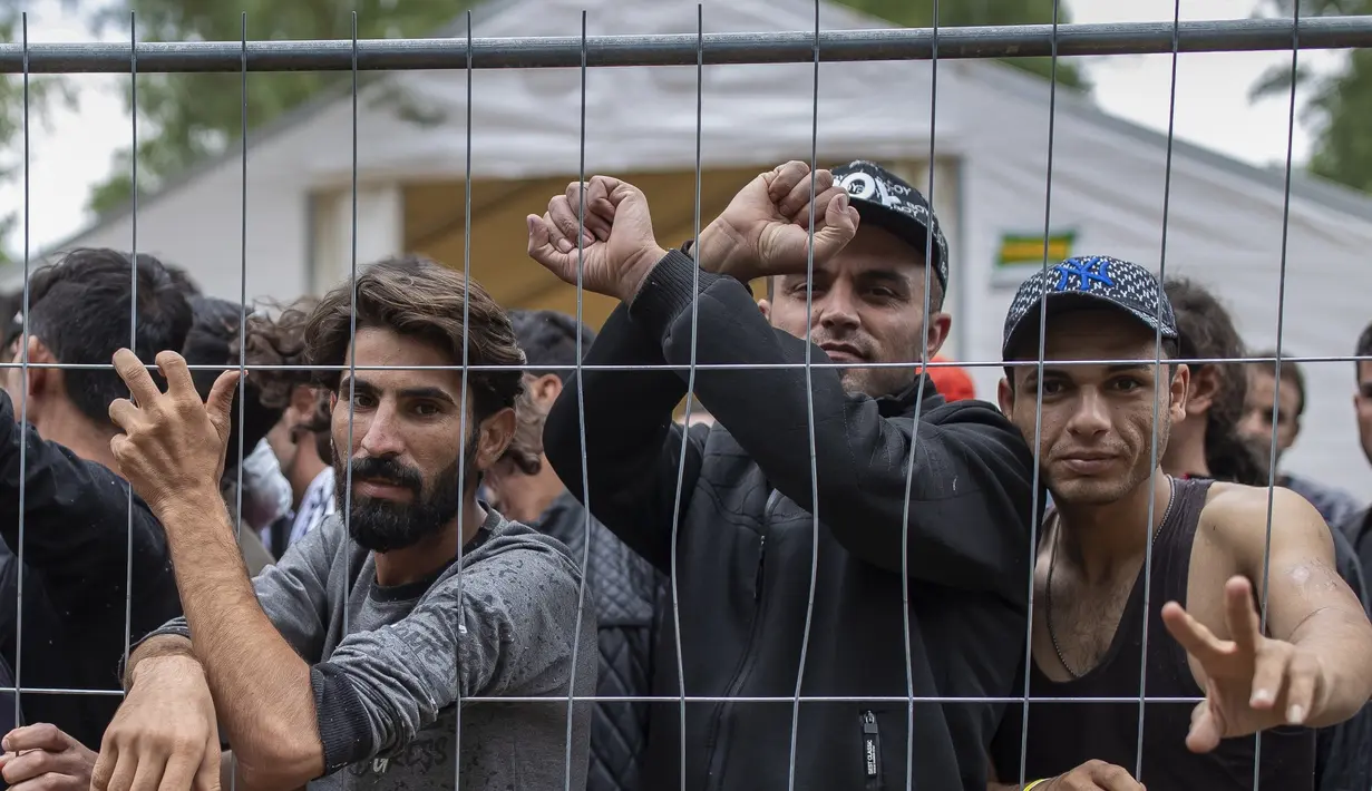 Para migran berdiri di belakang pagar di dalam kamp pengungsi yang baru dibangun di tempat latihan militer Rudninkai, sekitar 38km (23,6 mil) selatan dari Vilnius, Lituania, Rabu (4/8/2021). (AP Photo/Mindaugas Kulbis)