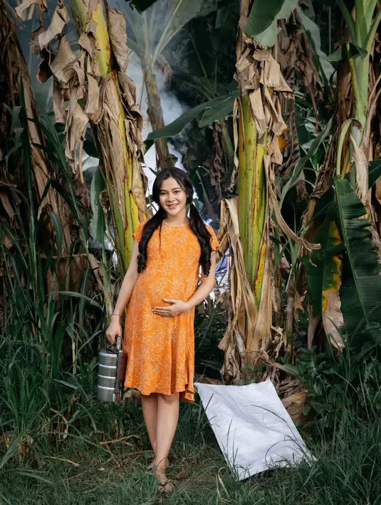 Berlatarkan perkebunan di sebuah pedesaan, Bella Bonita tampil sederhana dengan daster berwarna kuning.  [@bellabonita_r.a/@denny_caknan]