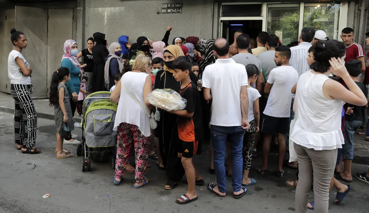 Seorang anak meninggalkan toko roti saat orang-orang menunggu giliran, di lingkungan Nabaa, Beirut, (13/8/2021). Tanpa masker, warga Lebanon berbondong-bondong ke toko roti sebelum fajar untuk membeli roti yang terjangkau ketika pasokan bahan bakar dan obat-obatan terbatas. (ANWAR AMRO/AFP)