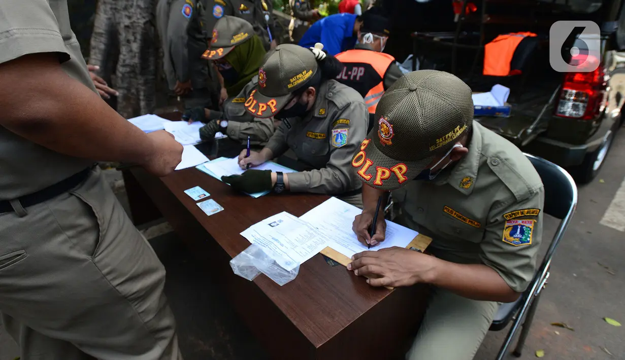 Petugas Satpol PP mendata warga yang terjaring razia pelanggar PSBB (Pembatasan Sosial Berskala Besar) di Pasar Gembrong, Jakarta, Selasa (2/6/2020). Para pelanggar aturan PSBB tersebut dijatuhi sanksi membayar denda atau melakukan pelayanan sosial. (merdeka.com/Imam Buhori)