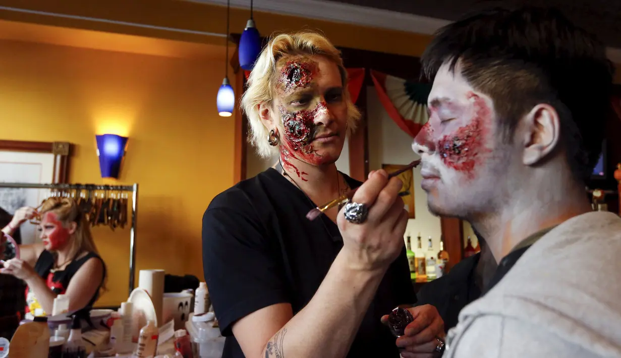 Seorang pria merias wajah rekannya untuk menyerupai zombie untuk menyambut halloween di Amerika, Minggu (18/10/2015). Tradisi Halloween berasal dar Irlandia yang dibawa hingga Amerika Serikat. (REUTERS/Shannon Stapleton)