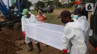 Petugas mengangkat peti jenazah Covid-19 untuk dimakamkan dengan prosedur covid 19 di TPU Tegal Alur, Jakarta, Minggu (3/12/2021). Sebanyak 625.518 kasus dinyatakan sembuh dan 22.555 orang meninggal dunia. (Liputan6.com/Angga Yuniar)