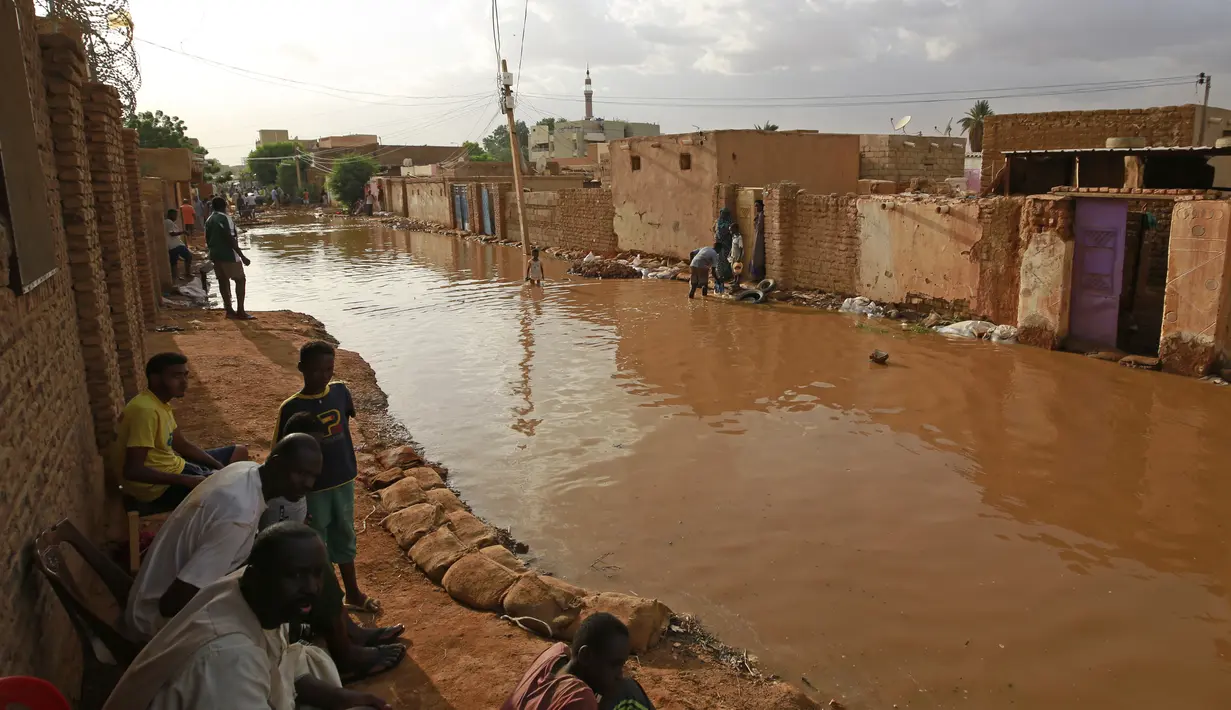 Penduduk Sudan duduk di luar rumah mereka yang banjir di daerah alqamayir di kota kembar ibu kota Omdurman (26/8/2020). (AFP Photo/Ashraf Shazly)