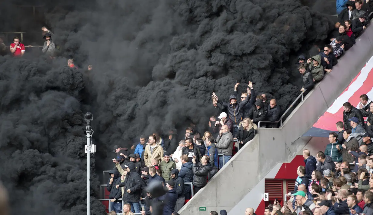 Penonton diselimuti asap hitam tebal saat pertandingan sepak bola PSV Eindhoven vs Ajax di Stadion Philips, Belanda (23/4). Asap tebal itu memaksa wasit untuk menunda pertandingan selama beberapa menit. (Olaf KRAAK / ANP / AFP)