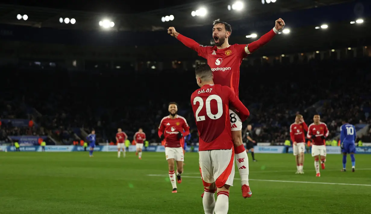 Gelandang Manchester United, Bruno Fernandes melompat ke pelukan Diogo Dalot saat merayakan gol ketiga mereka pada pertandingan pekan ke-29 Premier League 2024/2025 melawan Leicester City di King Power Stadium, Inggris pada 16 Maret 2025 waktu setempat atau Senin (17/3/2025) dini hari WIB. (Adrian Dennis/AFP)