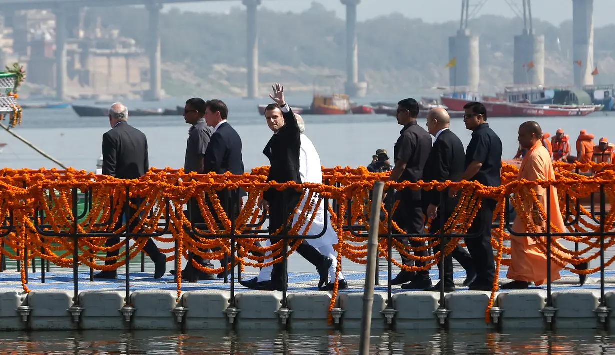 Presiden Prancis Emmanuel Macron melambaikan tangan saat akan naik perahu di Sungai Gangga di Varanasi, India, Senin (12/3). Kedatangan kedua pemimpin ini disambut sejumlah penduduk lokal. (AP Photo/Rajesh Kumar Singh)
