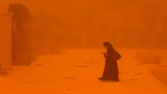 Seorang perempuan melihat-lihat telepon saat berjalan di tengah badai debu yang parah di Kota Kuwait pada 23 Mei 2022. Kabut oranye tebal telah menyelimuti Kuwait pada hari Senin, menyebabkan penerbangan ke dan dari bandara internasional negara itu ditangguhkan sementara, kata regulator penerbangan sipil. (Yasser Al-Zayyat / AFP)