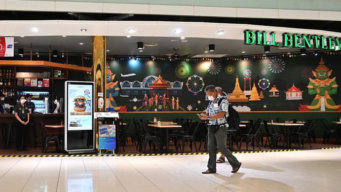 Pelancong  melintasi sebuah restoran kosong karena jumlah pengunjung menurun drastis di aula transit Bandara Suvarnabhumi di Bangkok, Rabu (11/3/2020). Di Thailand sendiri lebih dari 50 orang terinfeksi virus corona COVID-19 yang telah menggemparkan seluruh dunia. (Mladen ANTONOV/AFP)