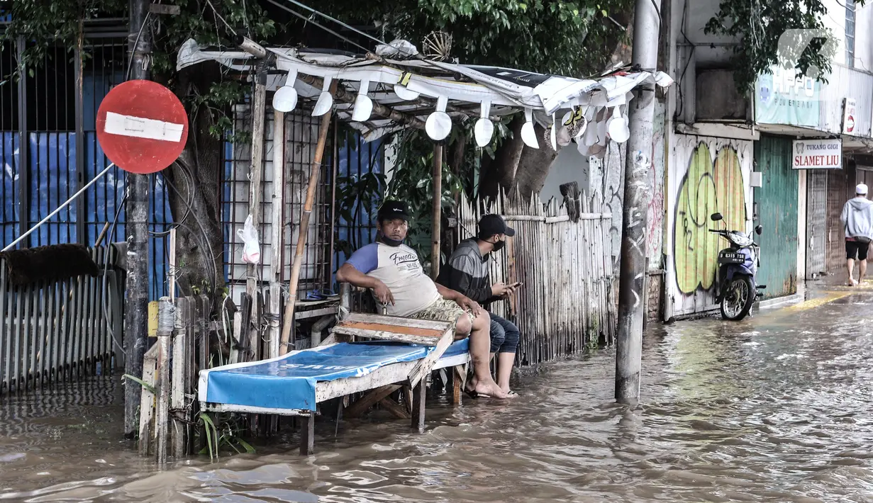 Warga duduk di sebuah pos saat banjir menggenangi Jalan Jatinegara Barat, Jakarta, Senin (8/2/2021). Selain menyebabkan pertokoan di kawasan itu terpaksa tutup, banjur juga menggangu aktivitas warga. (merdeka.com/Iqbal S. Nugroho)
