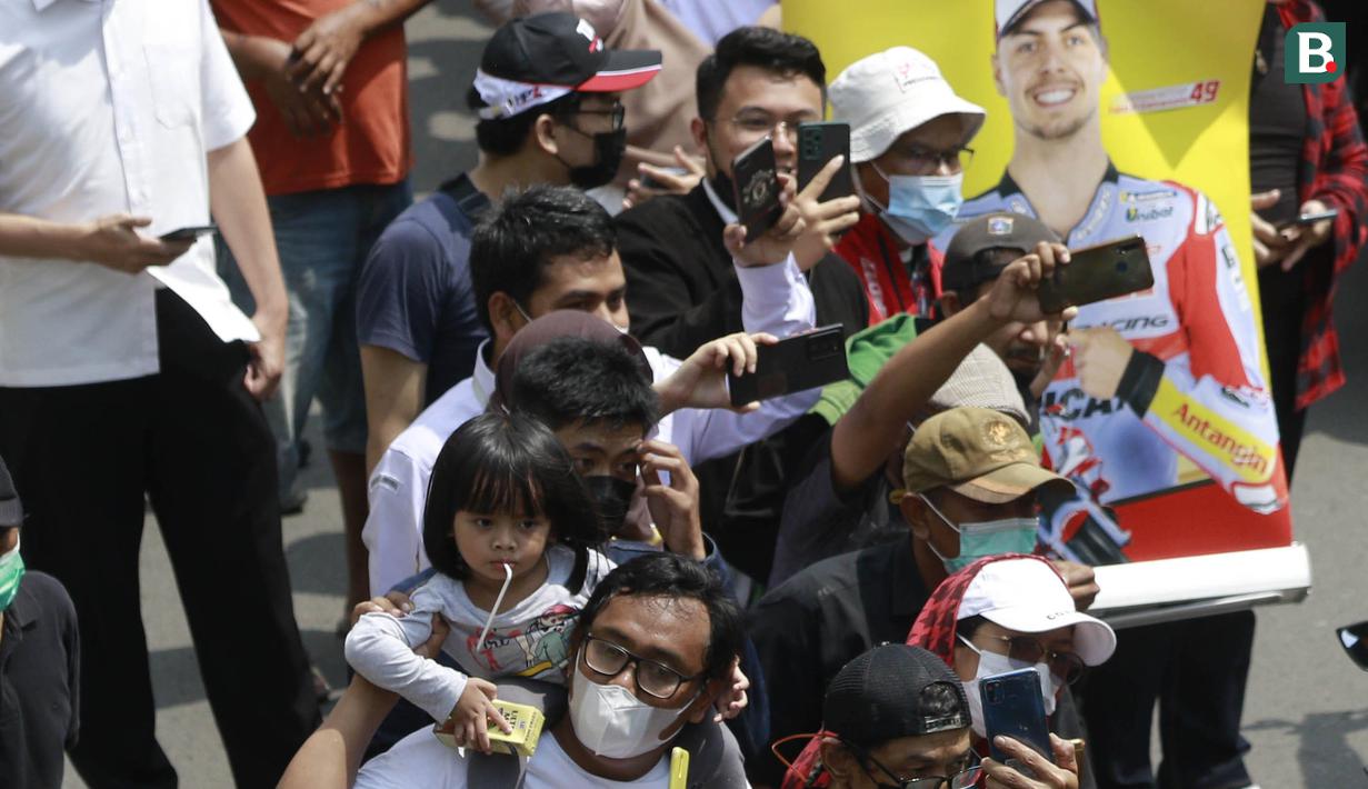 Seorang anak digendong orang tuanya saat melihat parade pembalap MotoGP di depan Sarinah Thamrin, Jakarta Pusat. Sebanyak 20 pembalap melakukan parade motor dari Istana Merdeka menuju Hotel Kempinski di Bundaran HI Jakarta Pusat, Rabu (16/03/2022). (Bola.com/M Iqbal Ichsan)
