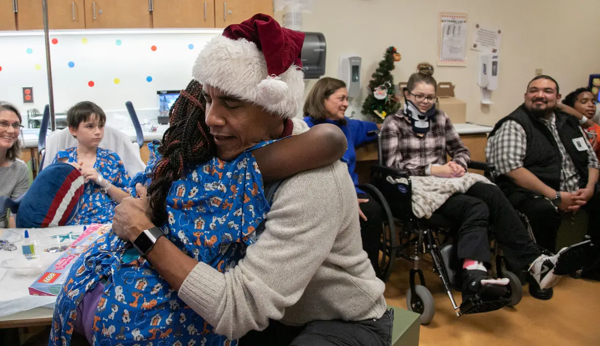 Mantan Presiden AS, Barack Obama memeluk seorang pasien anak di Children's National Medical Center , Washington, Rabu (19/12). Kedatangan Obama yang menyerupai sinterklas itu untuk membagikan hadiah natal kepada anak-anak di sana. (Chuck Kennedy / AFP)