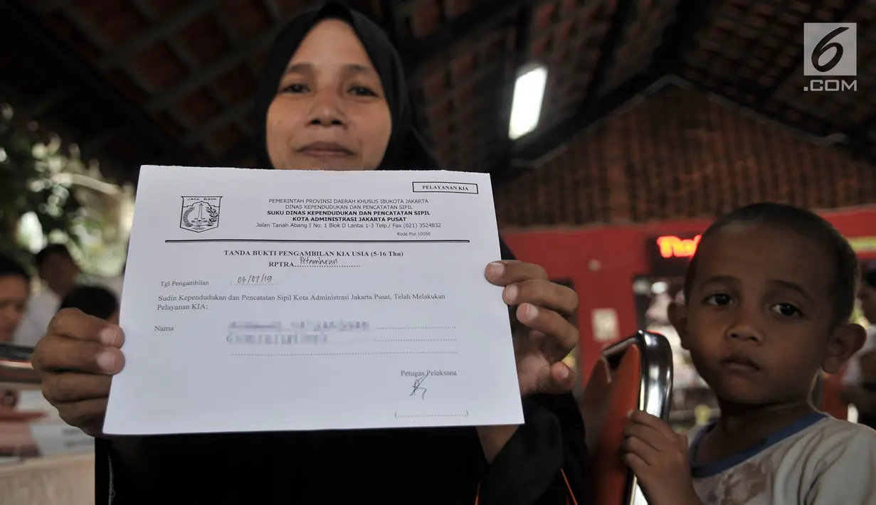 Warga didampingi anaknya menunjukkan tanda bukti pembuatan KIA saat pelayanan Bina Kependudukan di Rusun Petamburan, Jakarta, Rabu (26/6/2019). Pendataan ini melayani warga untuk membuat KTP elektronik, Kartu Identitas Anak (KIA), dan akte kelahiran. (merdeka.com/Iqbal S. Nugroho)