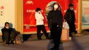 Warga yang memakai masker beristirahat dekat poster propaganda di alun-alun luar stasiun kereta api di Beijing, China, Kamis (8/12/2022). Di bawah pedoman baru yang diumumkan oleh Komisi Kesehatan Nasional China, frekuensi dan ruang lingkup pengujian PCR - yang telah lama menjadi andalan kehidupan yang membosankan dalam kebijakan nol-COVID China - akan dikurangi. (AP Photo/Ng Han Guan)