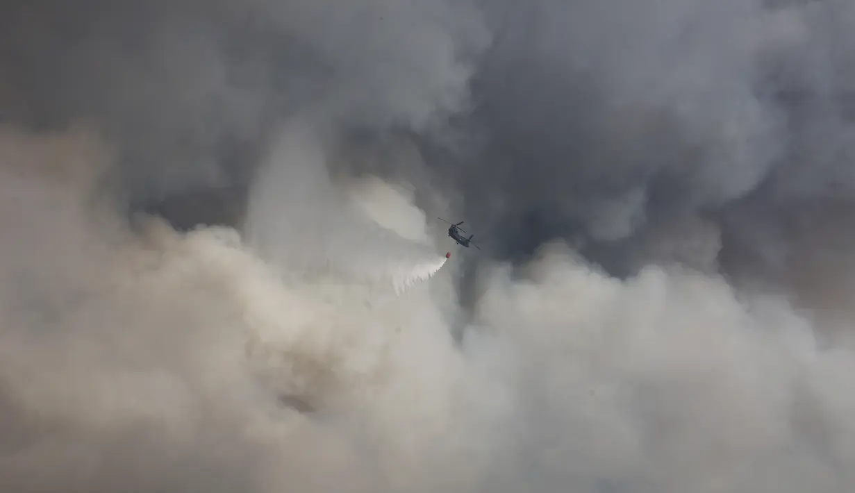 Helikopter militer menjatuhkan air di atas kebakaran hutan di pinggiran Voula, di selatan Athena, Yunani, Sabtu, 4 Juni 2022. Awan asap tebal imbas dari kebakaran hutan itu pun menganggu aktivitas di wilayah pinggiran selatan Yunani. (AP Photo/Yorgos Karahalis)