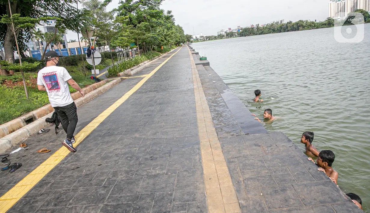 Seorang pria melihat anak-anak berenang di Danau Sunter, Jakarta, Selasa (2/2/2021). Minimnya lahan bermain anak membuat mereka memanfaatkan tempat yang tidak semestinya untuk bermain karena adanya risiko hanyut dan tenggelam bila tidak mampu untuk berenang. (Liputan6.com/Faizal Fanani)