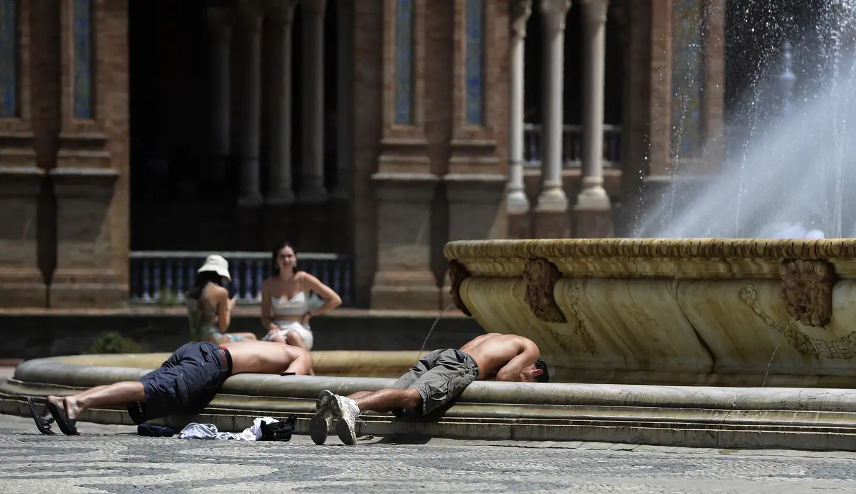 Dua pemuda membenamkan kepala mereka ke dalam air mancur untuk mendinginkan diri, di alun-alun Plaza de Espana di Seville, Spanyol pada 7 Agustus 2023. (CRISTINA QUICLER / AFP)