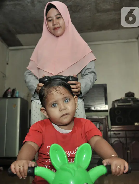 Fauziah Afiqa bermain sepeda bersama ibunya di kediamannya di Kampung Bulak Sentul, Harapan Jaya, Bekasi, Jawa Barat, Kamis (10/10/2019). Orangtua Afiqa mengatakan anaknya bermata biru sejak usia 8 bulan. (merdeka.com/Iqbal Nugroho)
