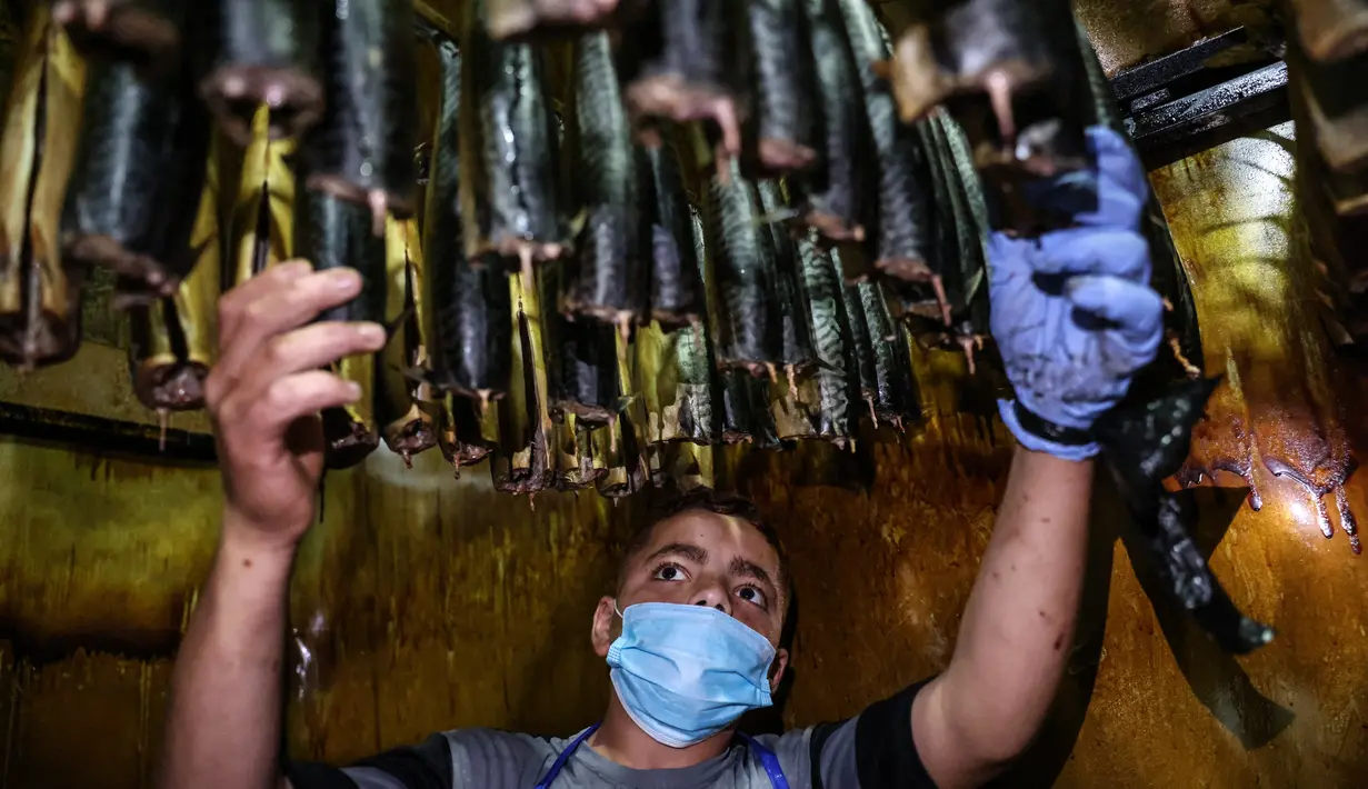 Seorang pemuda Palestina mengasapi makarel untuk dijual di pasar ikan menjelang liburan Idul Fitri di kota Rafah di Jalur Gaza selatan (3/5/2021). Ikan asap makarel menjadi salah satu menu hidangan buka puasa terfavorit bagi warga Gaza selama Ramadhan. (AFP/Said Khatib)
