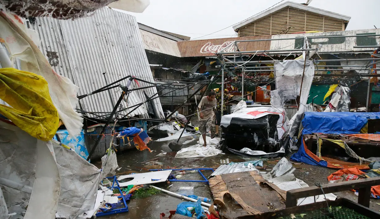Warga berjalan di samping bangunan yang roboh akibat Topan Mangkhut di kota Tuguegarao, Cagayan, Filipina (15/9). Pengamat cuaca memperkirakan angin kemungkinan menimbulkan gelombang tinggi hingga 6 meter dan menghantam desa-desa. (AP Photo/Aaron Favila)