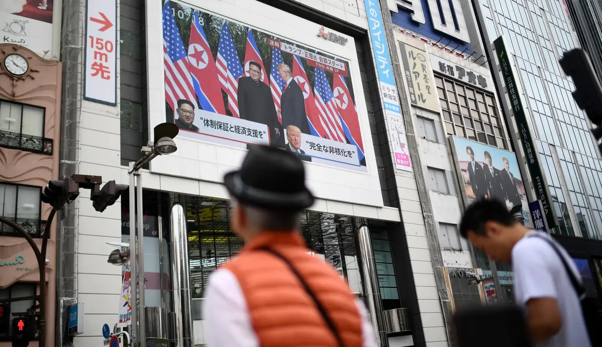 Pejalan kaki melihat layar yang menampilkan pertemuan antara pemimpin Korea Utara Kim Jong-un dan Presiden AS Donald Trump di Tokyo, Selasa (12/6). Untuk pertama kalinya dalam sejarah, Donald Trump dan Kim Jong-un bertemu. (AFP PHOTO/Martin BUREAU)