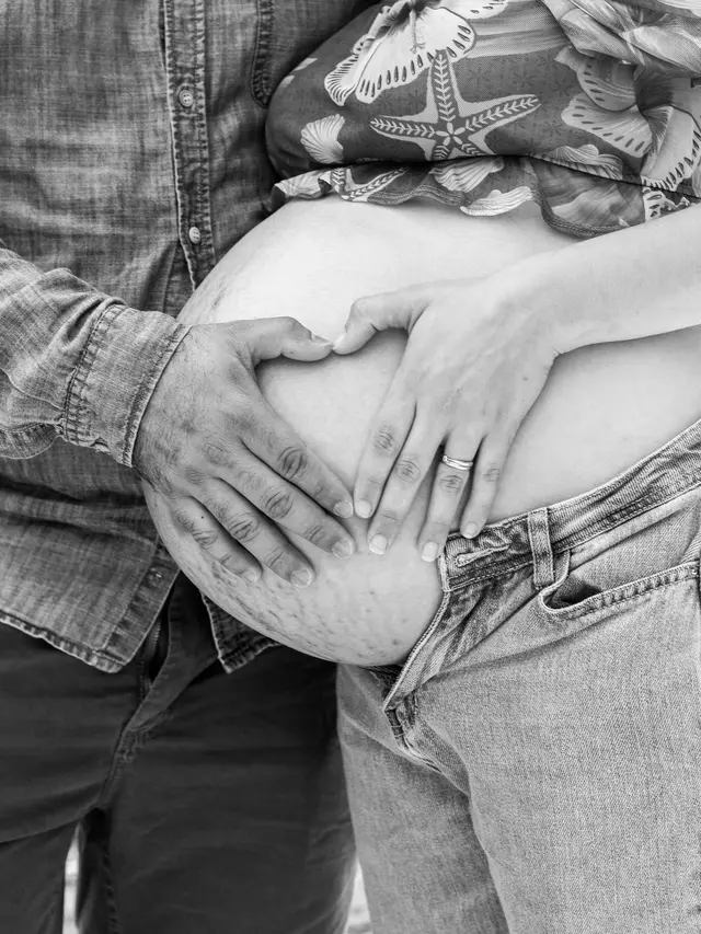 Suami memegang perut istrinya yang tengah hamil besar dengan guratan stretch mark di bagian bawahnya