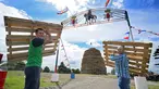 Dua orang pria membawa palet kayu yang akan disusun untuk membuat api unggun di Ballymacash, Lisburn, Irlandia (10/7). Api unggun raksasa ini dinyalakan setiap tahun di Irlandia Utara pada malam 11 Juli. (AFP Photo/Paul Faith)