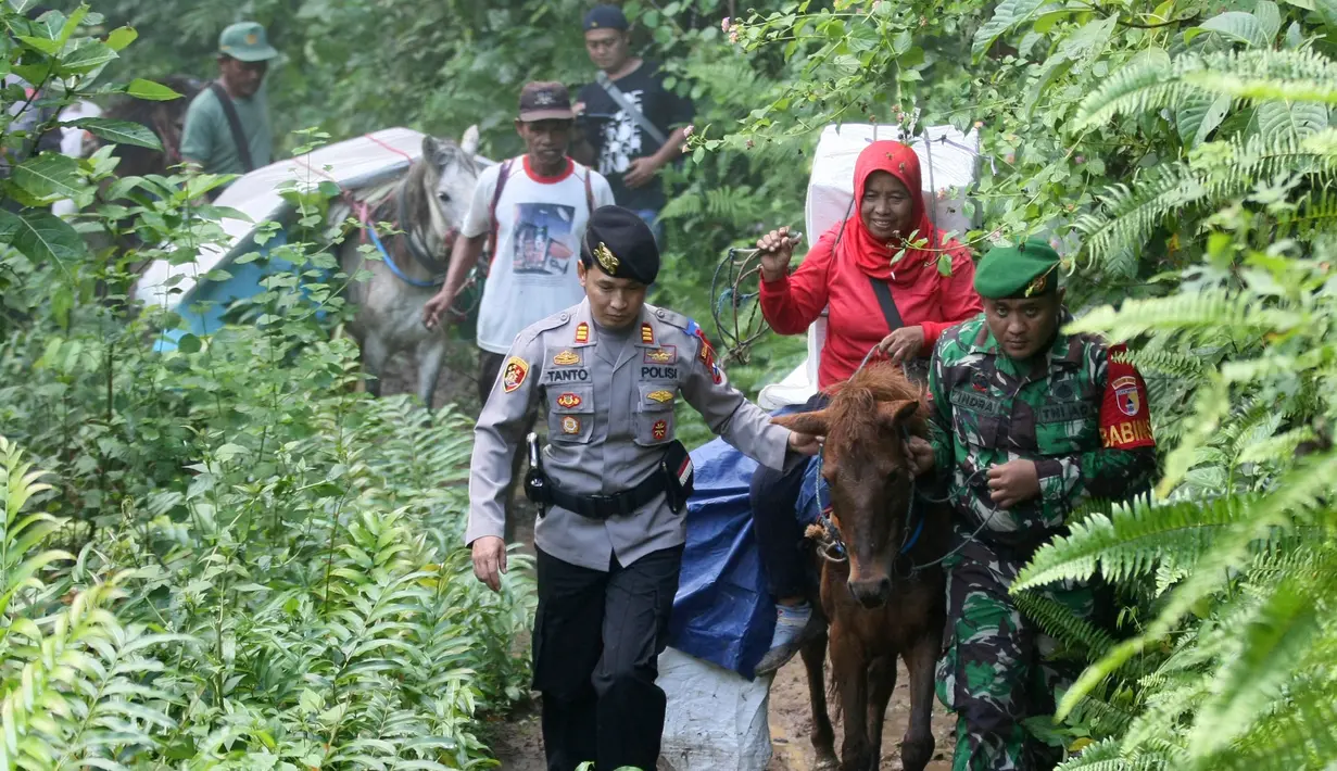 Polisi dan tentara mengawal petugas Pemilu 2019 yang menaiki kuda untuk mendistribusikan logistik ke TPS di desa-desa terpencil di Tempurejo, Jawa Timur, Senin (15/4). Petugas membawa kotak suara dan perlengkapan pemilu lainnya. (AP Photo/Trisnadi)
