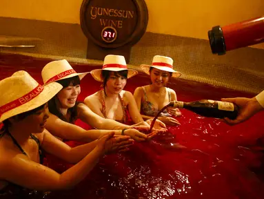 Seorang pria menuangkan anggur ke dalam tangan seorang wanita saat mereka duduk dalam air panas dengan air berwarna anggur di resor spa Hakone Kowaki-en Yunessun saat acara menandai Beaujolais Nouveau Day,Tokyo, Jepang (19/11). (REUTERS/Thomas Peter)