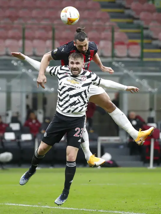 Pemain AC Milan Zlatan Ibrahimovic melompat di atas pemain Manchester United Luke Shaw untuk menyundul bola ke gawang pada pertandingan leg kedua babak 16 besar Liga Europa di Stadion San Siro, Milan, Italia, Kamis (18/3/2021). Manchester United  menang 1-0. (AP Photo/Antonio Calanni)
