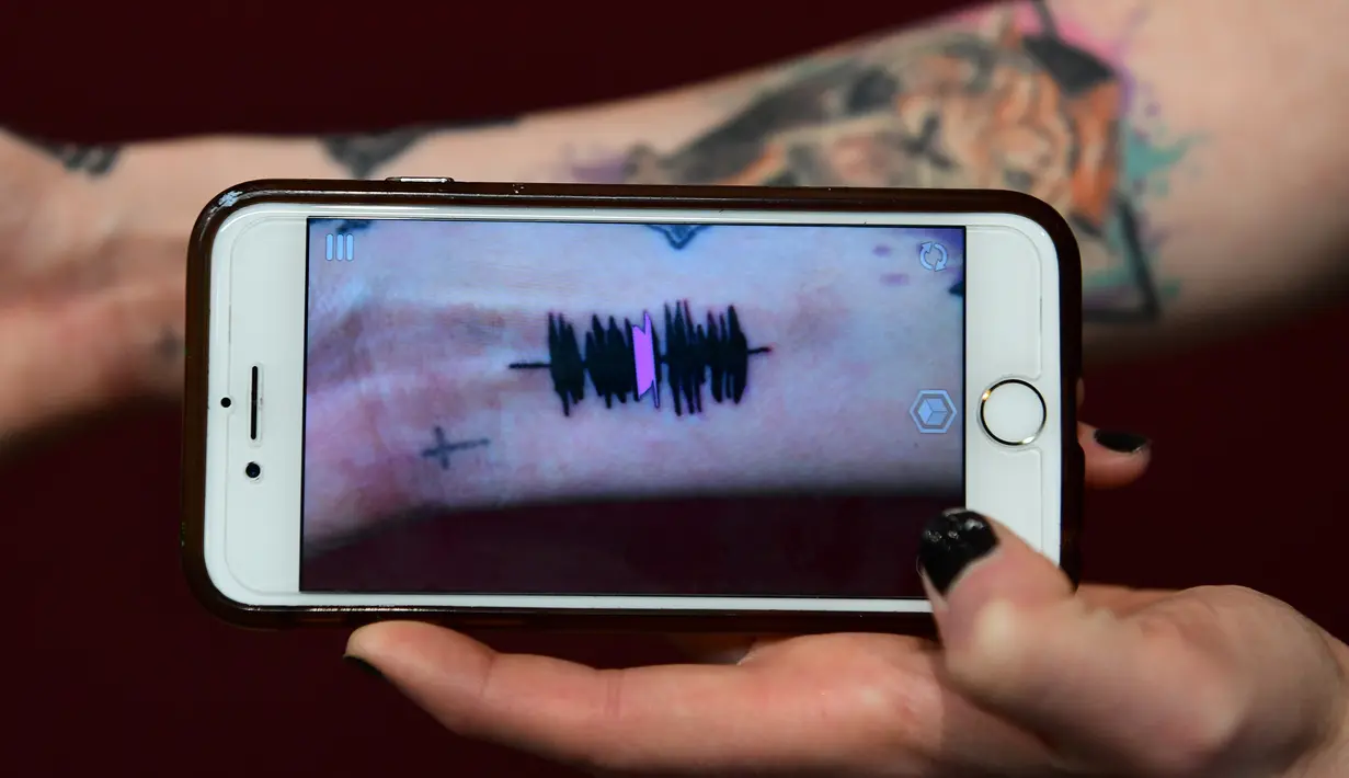 Hanna Washlake mendengarkan tato gelombang suara yang mengeluarkan pesan dari ibunya di Black Raven Tattoo California, 12 April 2018. Untuk mendengarkan Soundwave Tattoo yang perlu dilakukan memegang telepon kamera ke gambar tato. (AFP/FREDERIC J. BROWN)