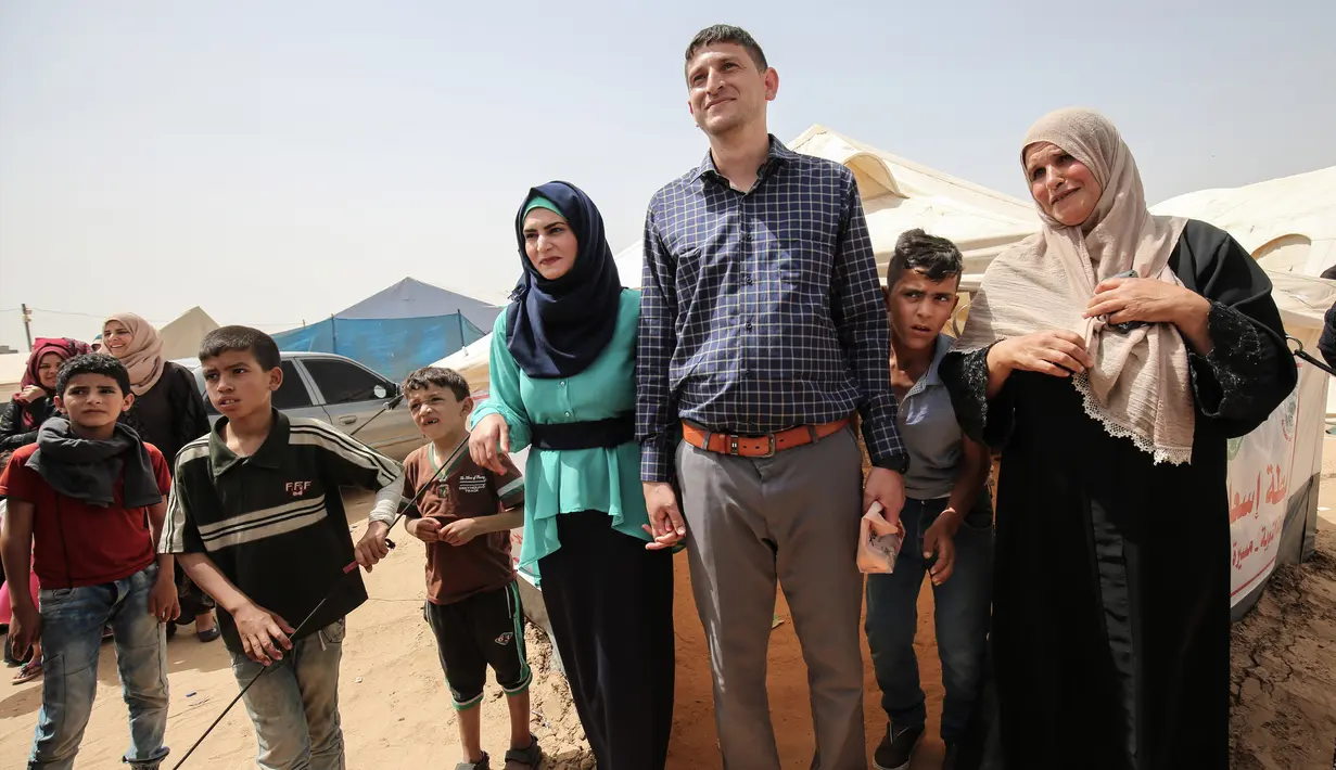 Pasangan petugas medis Muadh Al-Raqab (tengah) dan Hadeel Al-Najjar yang baru menikah berfoto di luar tenda di jalur Gaza selatan, Palestina (2/5). (AFP Photo/Said Khatib)