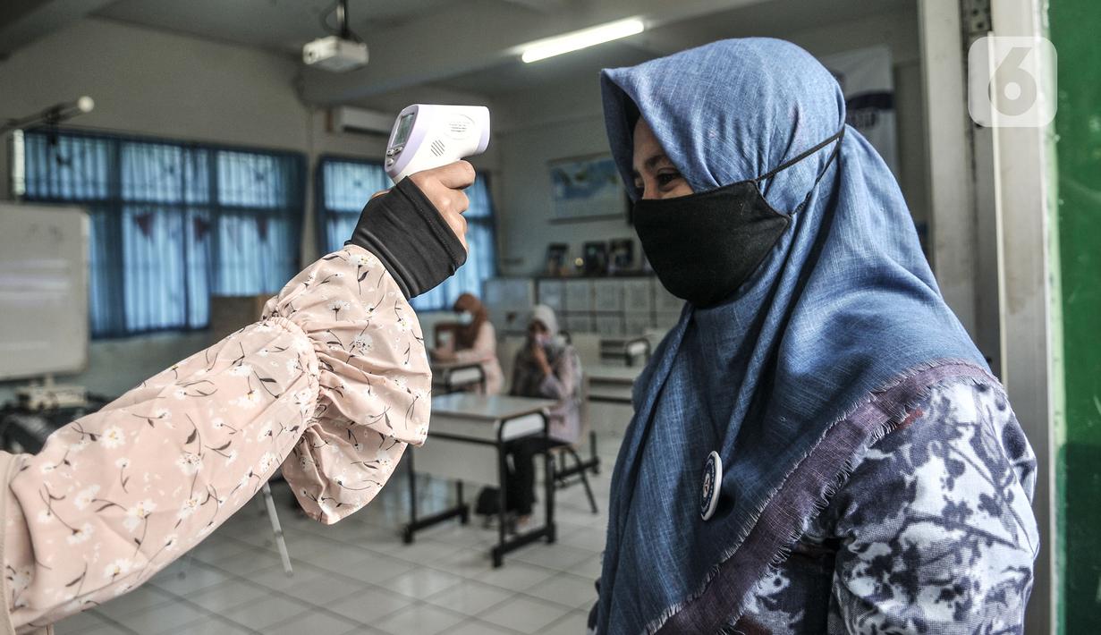 Guru diperiksa suhu sebelum memasuki ruang kelas saat sekolah dengan model Kelas Hybrid di SMPN 255, Jakarta, Selasa (30/3/2021). Simulasi kegiatan belajar mengajar (KBM) dengan model kelas Hybrid digelar terkait rencana sekolah tatap muka di awal tahun ajaran baru. (merdeka.com/Iqbal S Nugroho)